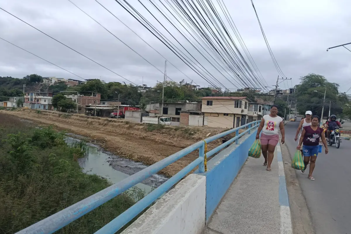 local 1 principal, Residentes de 4 de Noviembre caminan sobre el puente, desde donde se aprecia que la limpieza del cauce del río Manta está inconclusa. 